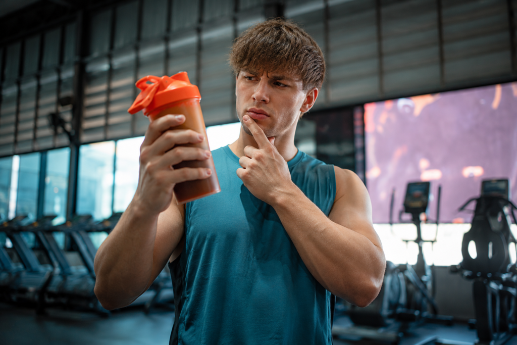 Deportista observando un shaker con whey protein blend en el gimnasio